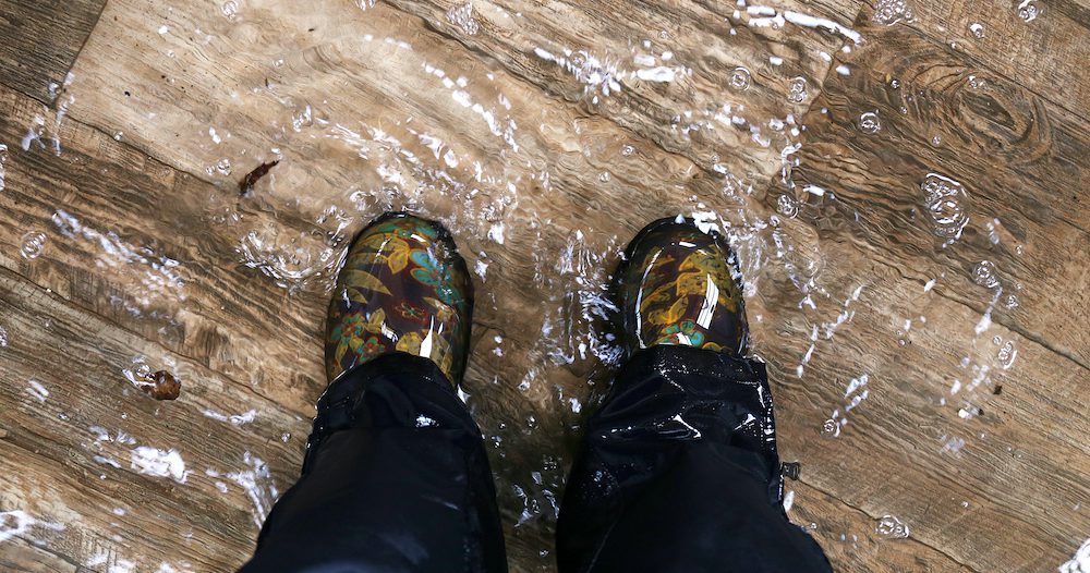 Woman's Feet Wearing Waterproof Boots, Standing in a Flooded House with Vinyl Wood Floors.