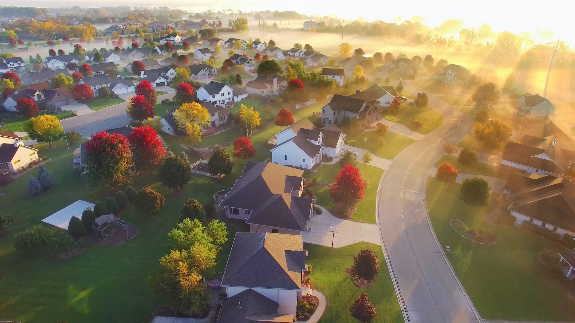Spectacular sunbeams through fog in autumn neighborhood, aerial view.