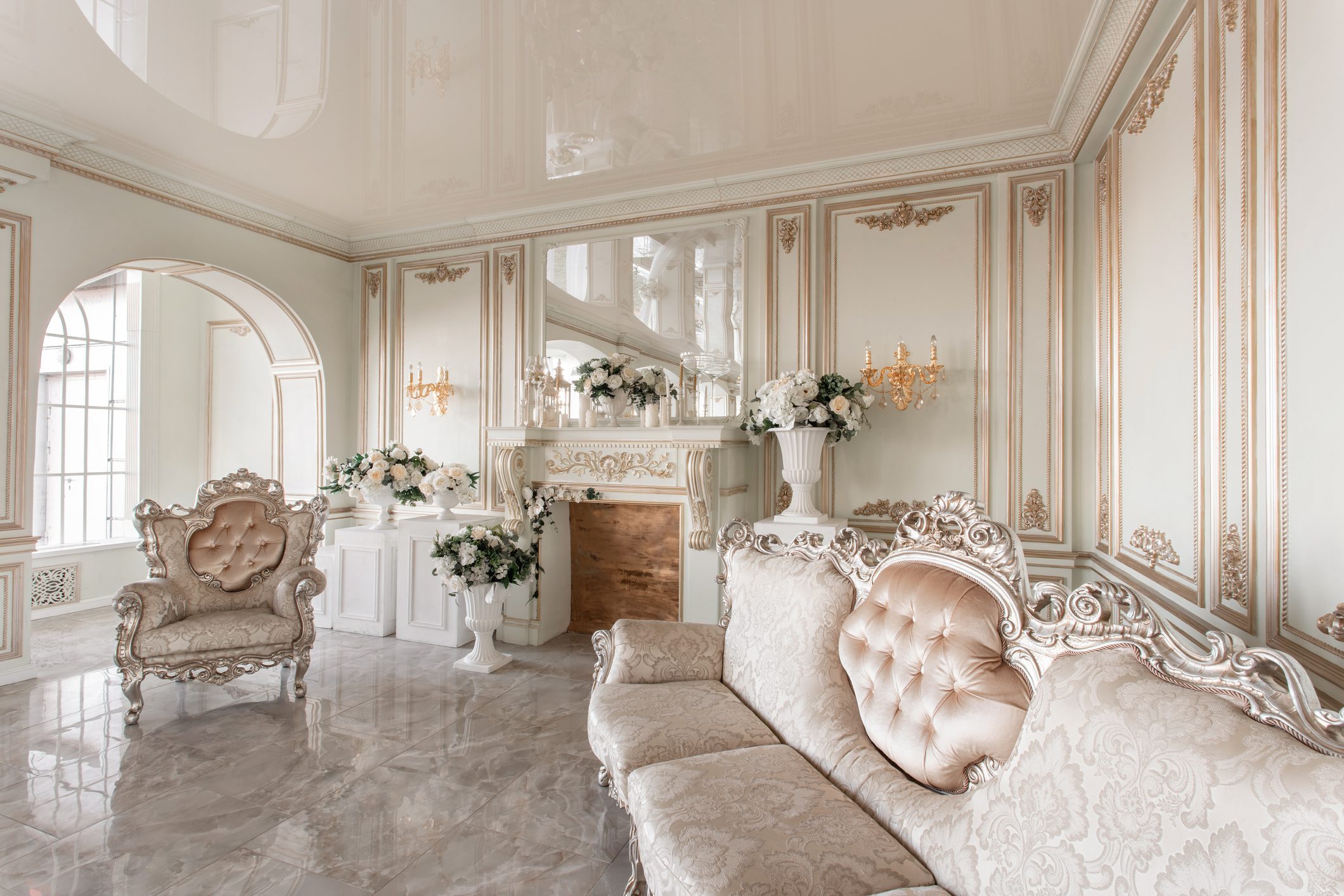 Morning in luxurious light interior in mansion . Bright and clean interior design of a luxury living room with stone floors, fireplace, sofa and chair . Stucco on walls